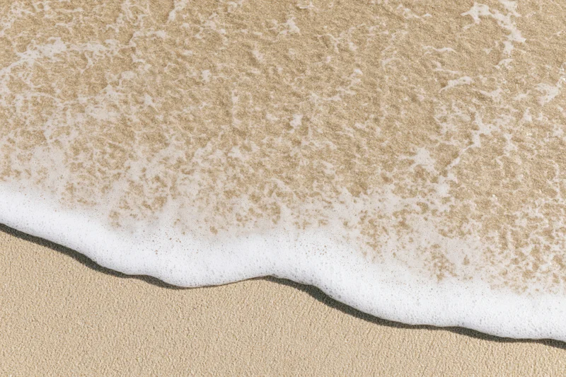 Shallow ocean wave foam washing over smooth wet sand from above