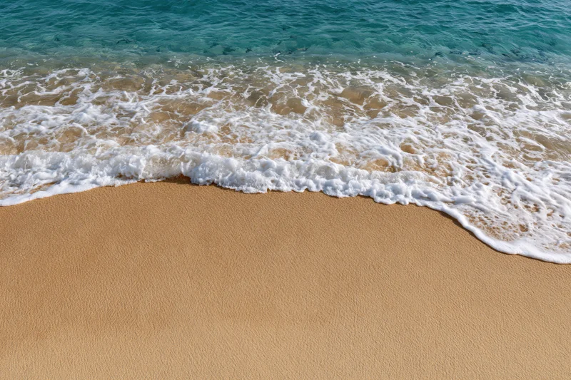 Shallow ocean wave with white seafoam washing over flat sandy beach