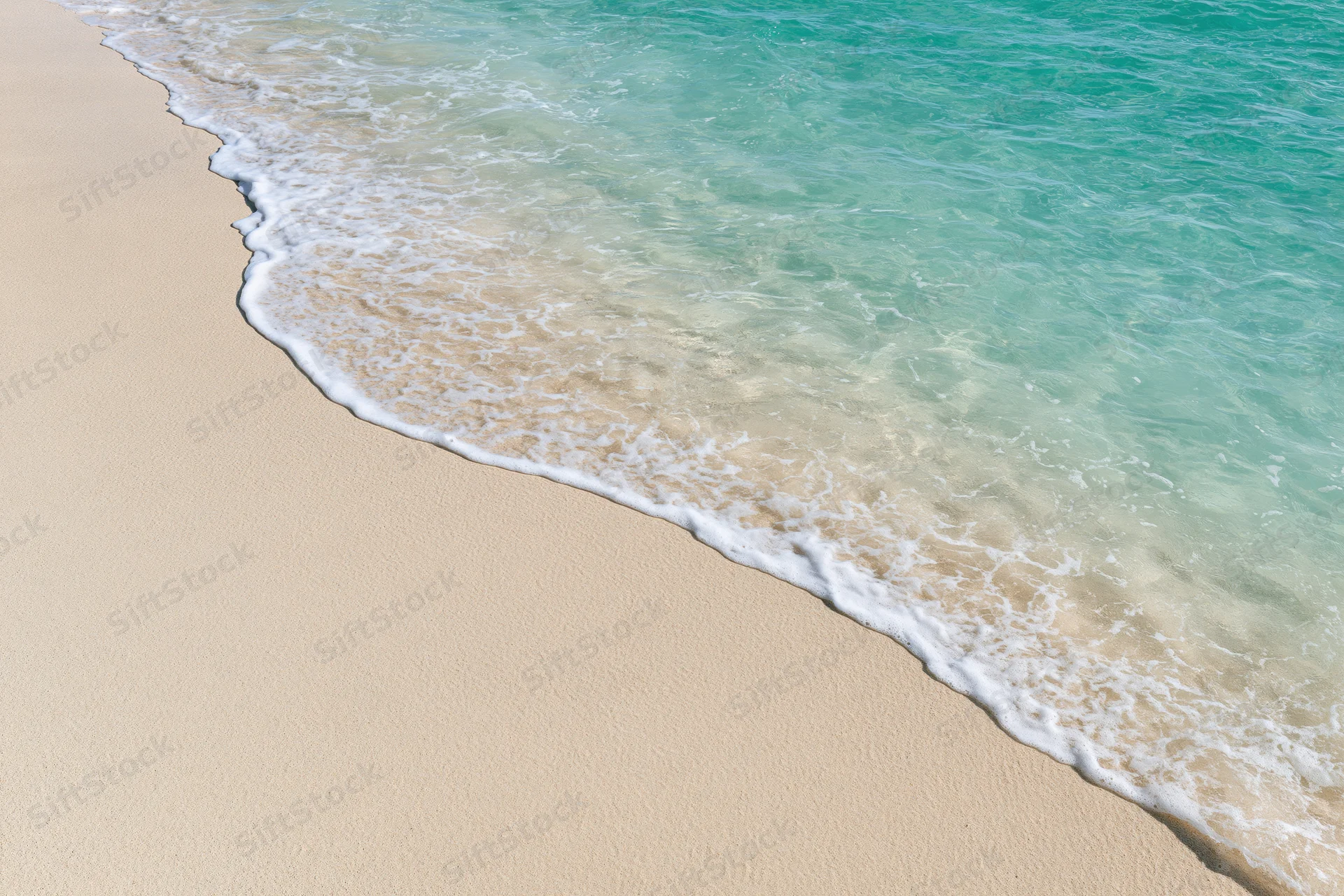 Turquoise ocean wave washing gently onto pale sandy beach