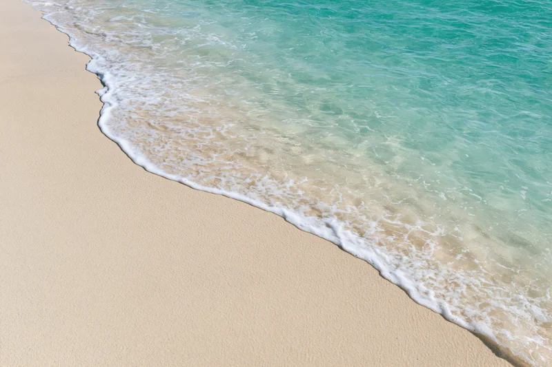 Turquoise ocean wave washing gently onto pale sandy beach