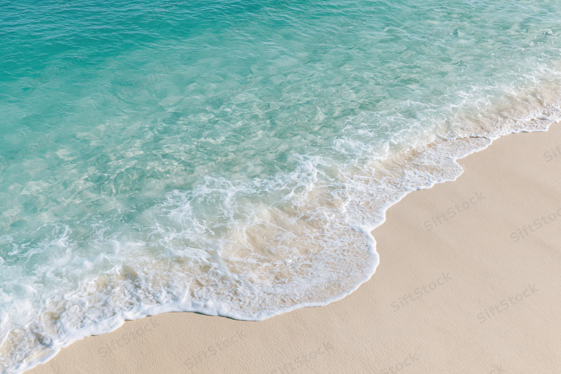 Turquoise ocean wave washing onto pale sandy beach