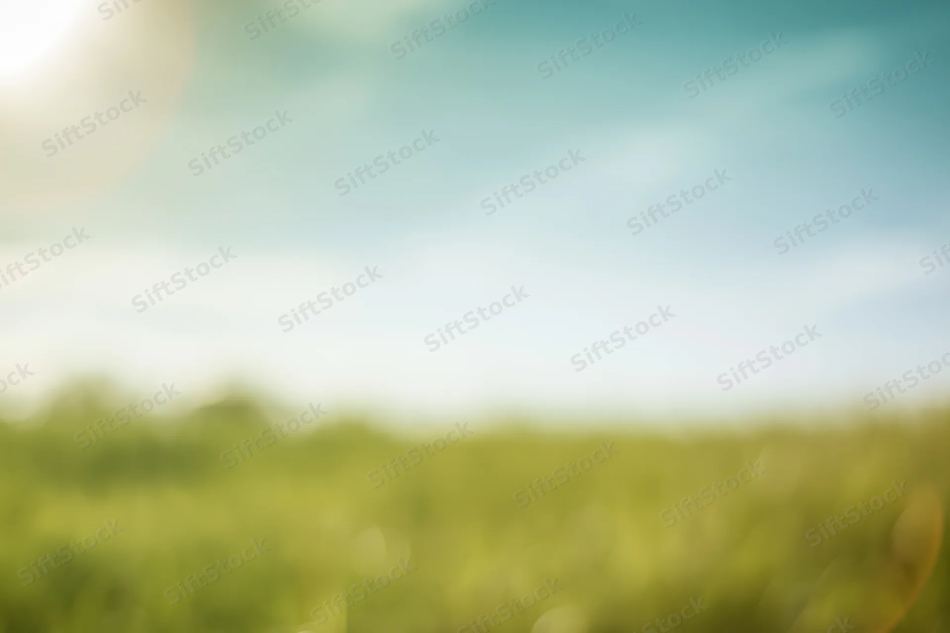 Blurred green field under blue sky with sunlight and bokeh effect