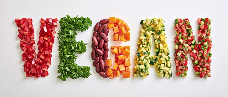 The word vegan spelled with chopped vegetables and herbs on a white surface