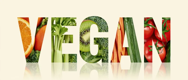 The word vegan spelled in bold letters filled with colorful fruits and vegetables on a reflective surface