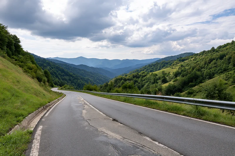 Winding asphalt road curving through green mountain valley under cloudy sky