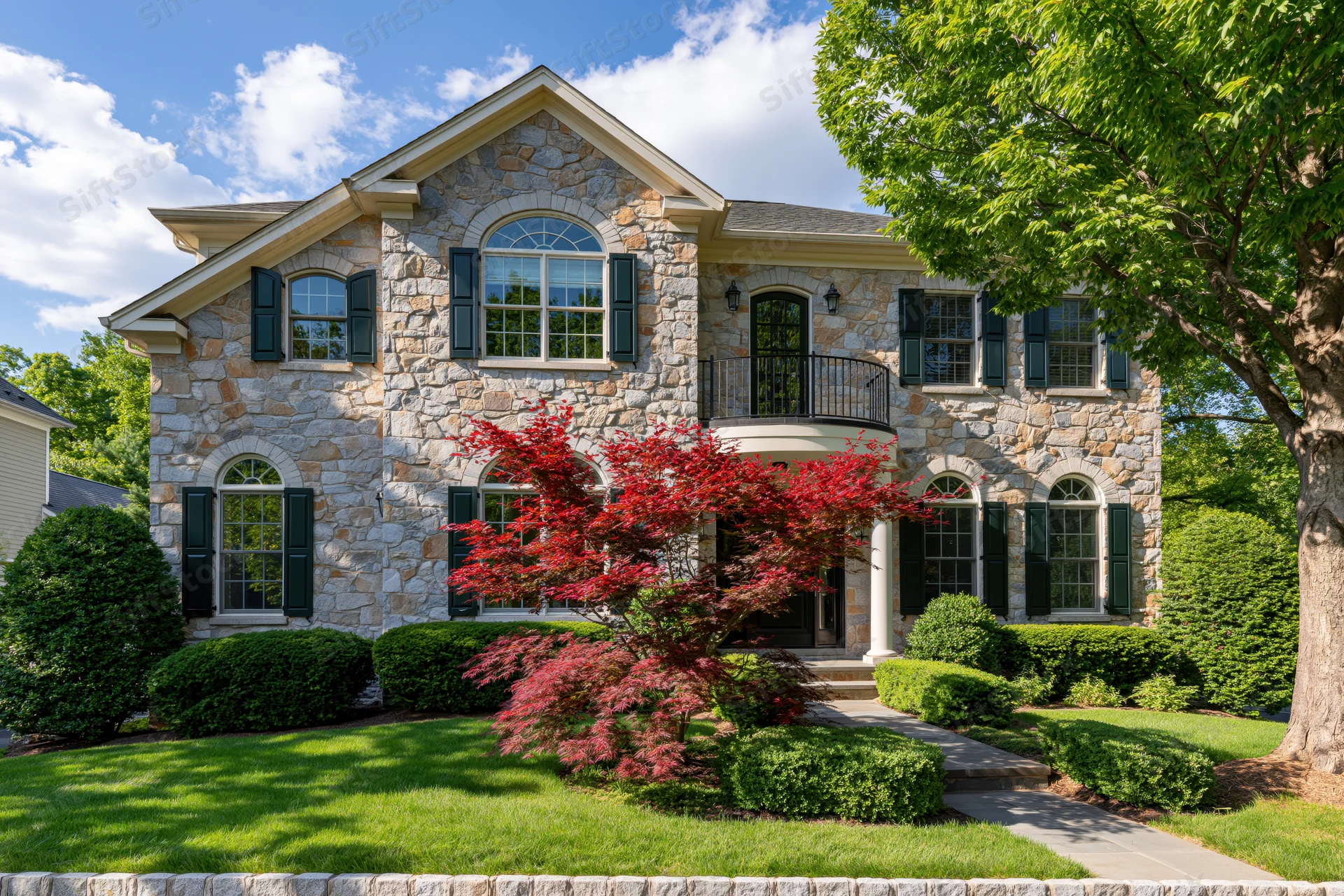 Two-story stone-facade suburban house with arched windows and green lawn in front yard