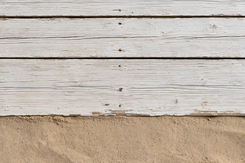 Weathered white-painted wooden planks meeting fine beach sand