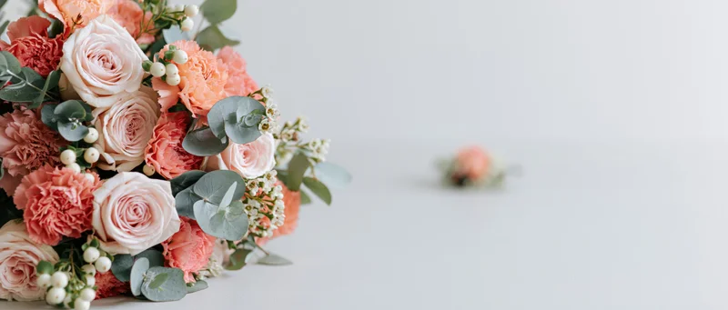 Wedding bouquet of blush and coral roses and carnations with eucalyptus leaves on white surface