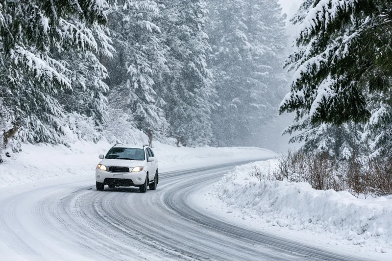 White suv driving on winding snow-covered road through snowy forest