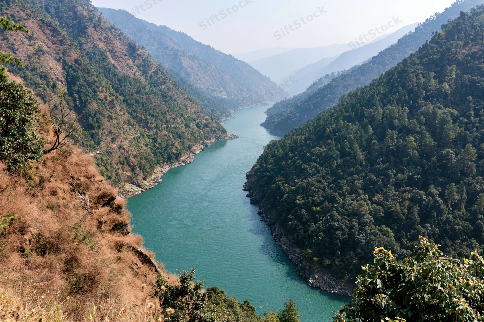 Turquoise river winding through a deep mountain valley with forested slopes and rocky cliffs