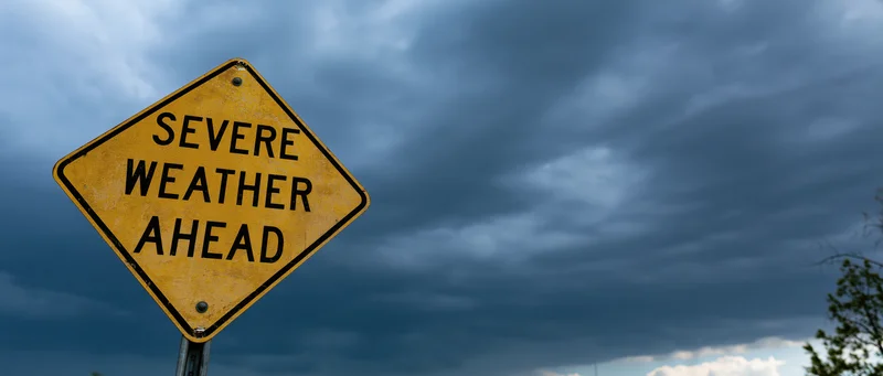 Yellow diamond-shaped road sign reading severe weather ahead against dark stormy sky