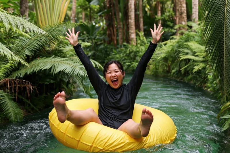 Woman floating in yellow inflatable ring on jungle river, arms raised in joy