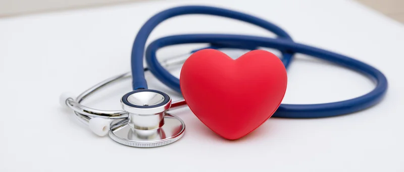 Blue chrome stethoscope lying beside red rubber heart on white surface