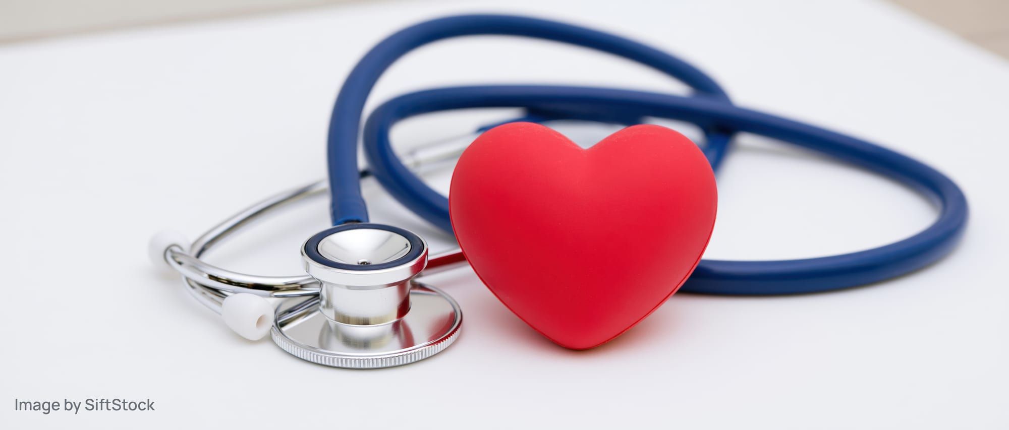 Blue chrome stethoscope lying beside red rubber heart on white surface