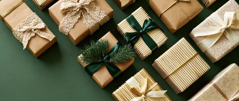 Wrapped gift boxes arranged on a dark green surface with ribbons and pine sprigs