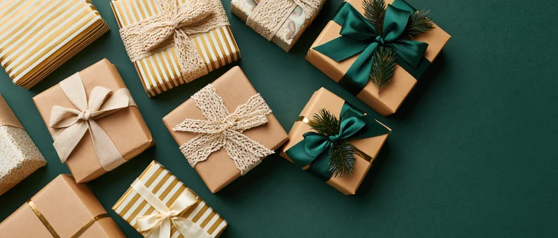 Wrapped gift boxes with ribbons and pine sprigs arranged on a dark green surface