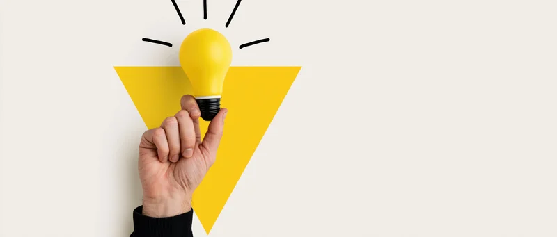 Hand holding yellow lightbulb against white background with graphic triangle and rays