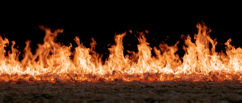 Horizontal wall of flames burning low against dark ground at night