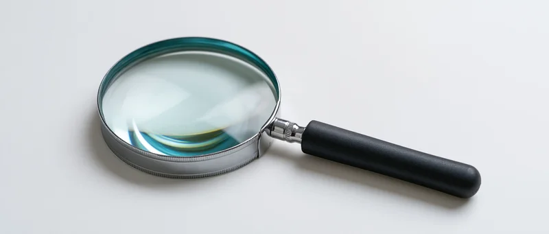 Magnifying glass with black handle and silver frame resting on white surface