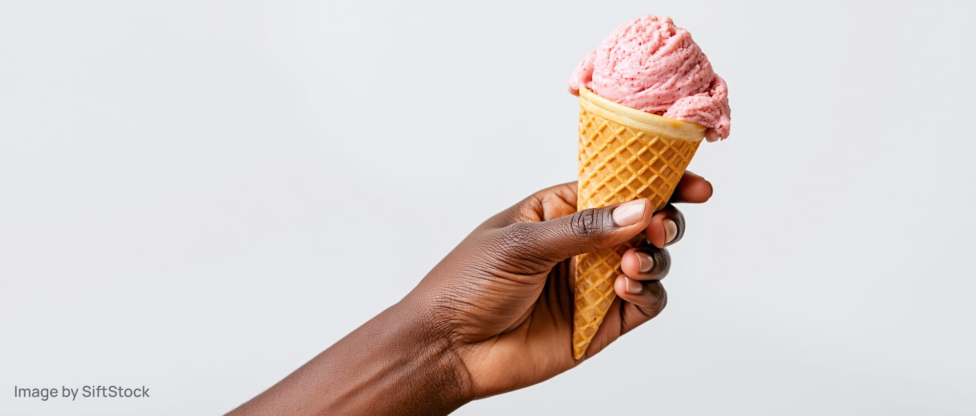 Dark-skinned hand holding a pink strawberry ice cream in a waffle cone against white background