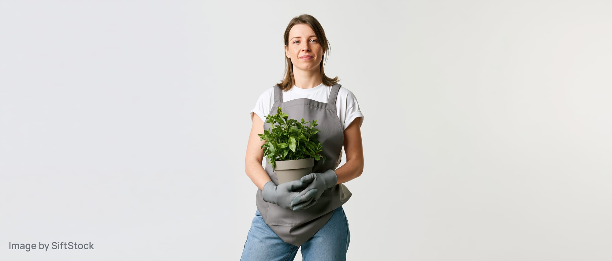 Woman in grey apron holding potted green plant in studio setting