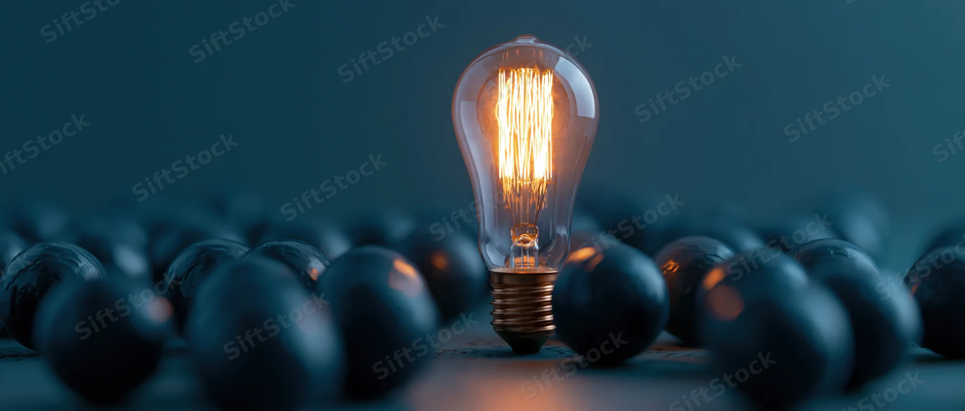 Single glowing edison filament lightbulb standing upright among unlit bulbs on dark surface