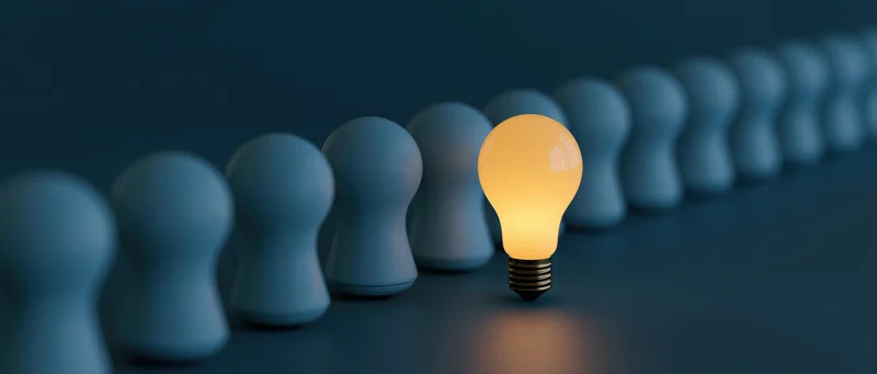Glowing lightbulb replacing a figure in a row of identical shapes on a dark surface