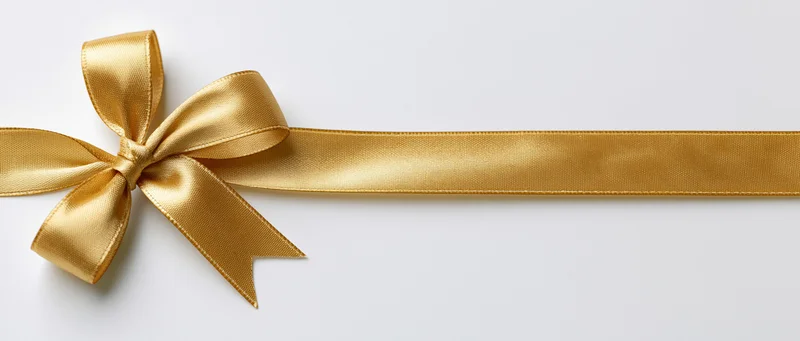 Gold satin ribbon tied in a bow lying horizontally on a white surface with copyspace