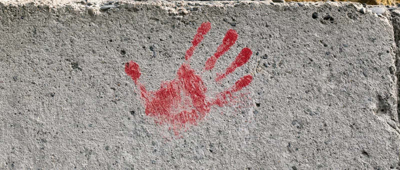 Red handprint painted on rough concrete wall outdoors