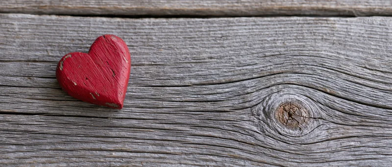 Red painted wooden heart resting on weathered wood surface