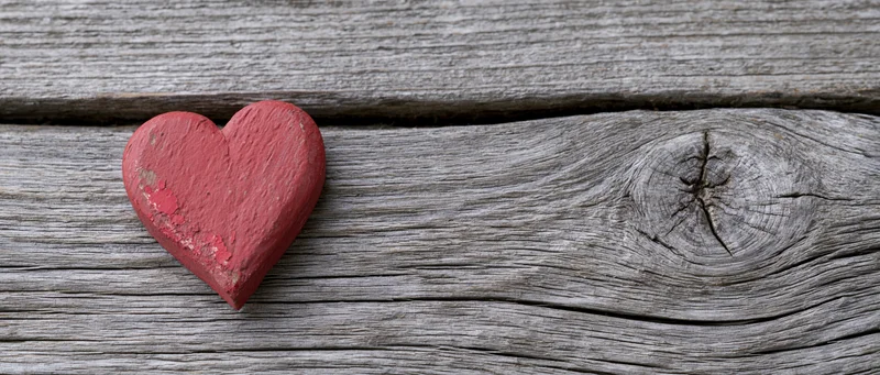 Red painted wooden heart resting on weathered wood surface