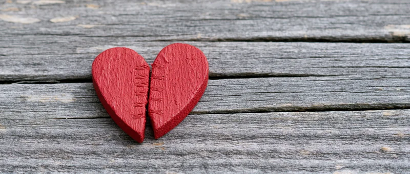 Broken red wooden heart with stitched seam resting on weathered wood planks