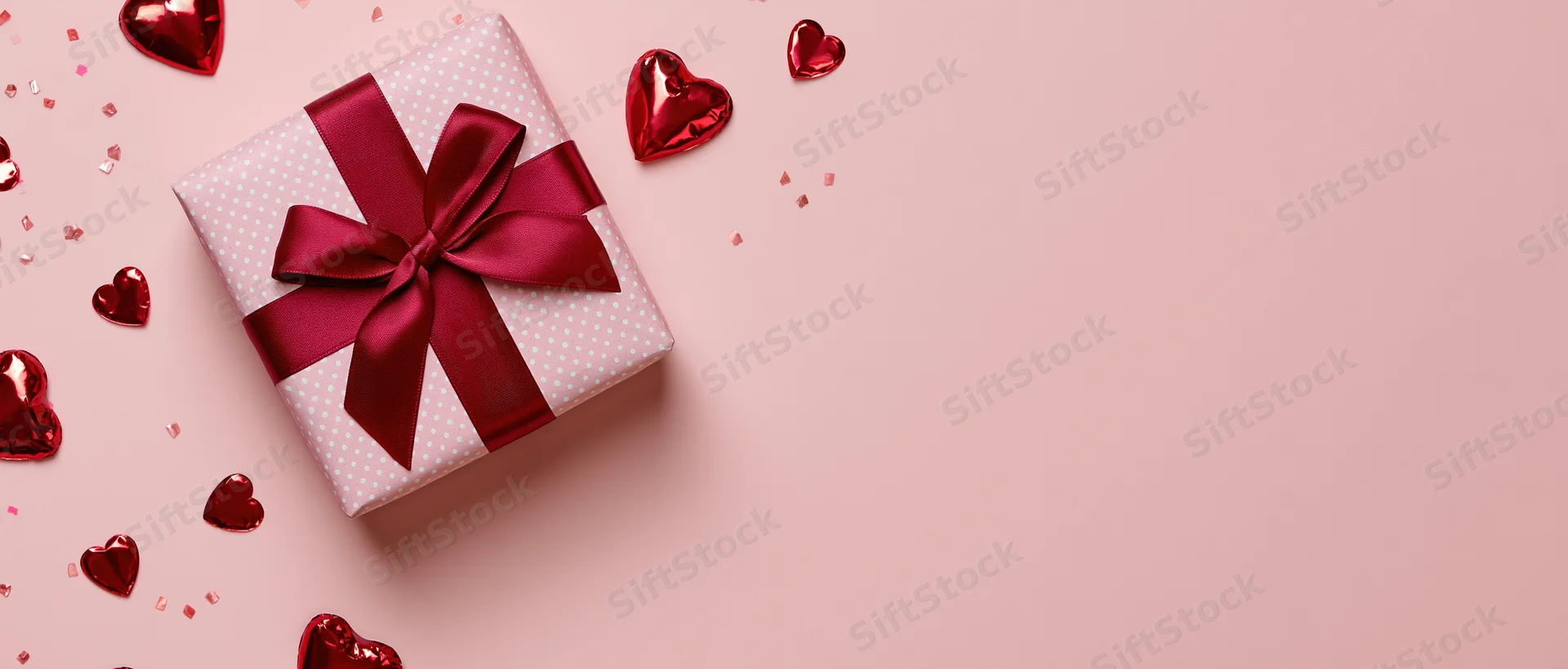 Wrapped gift box with red ribbon and heart decorations on pink background