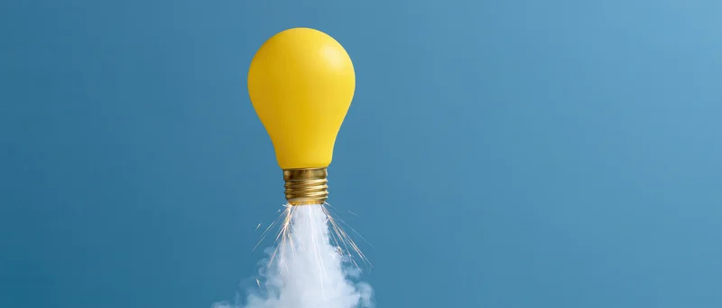 Yellow lightbulb launching upward with smoke and sparks against blue background