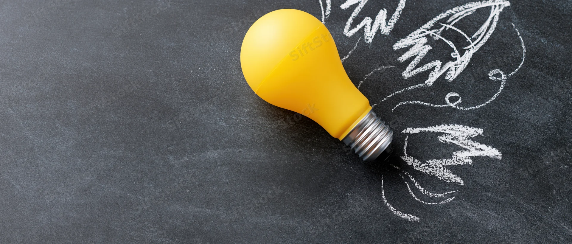 Yellow plastic lightbulb on dark chalkboard with chalk-drawn rocket and smoke trails