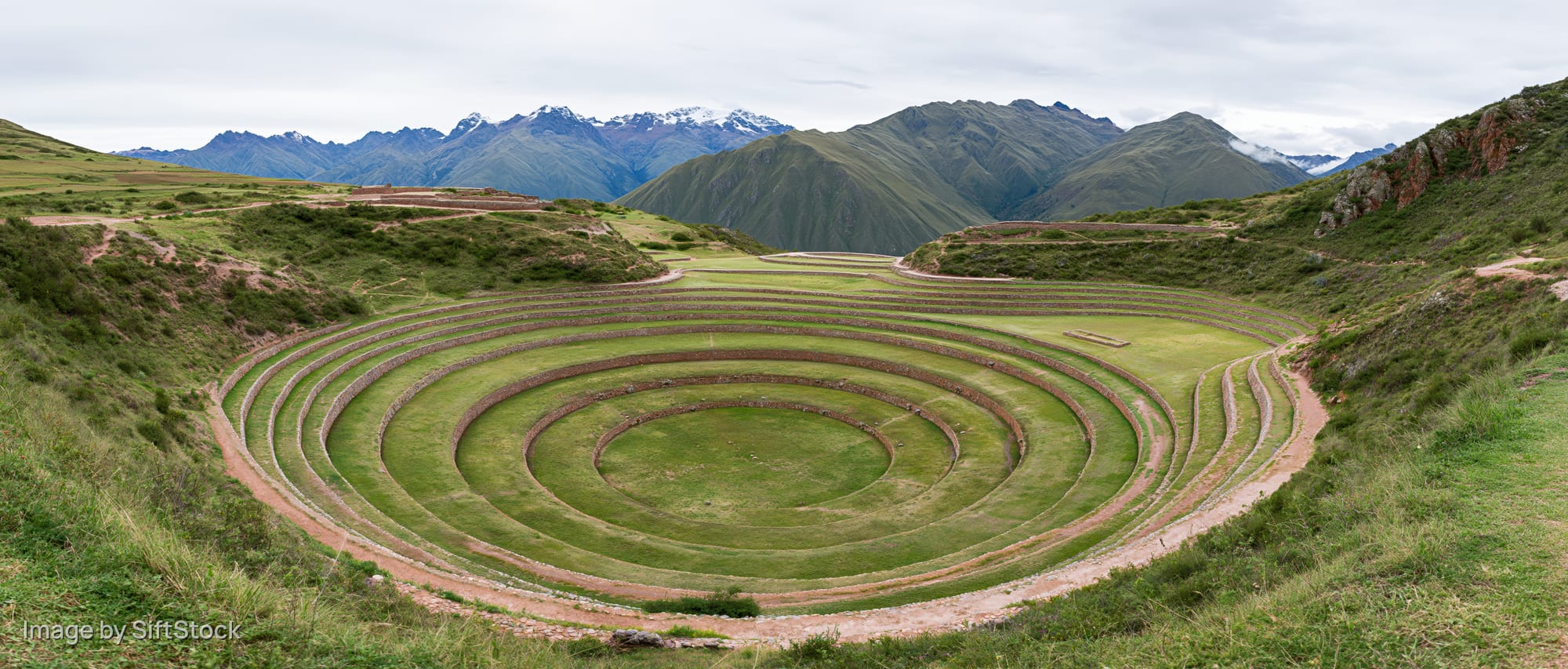 Circular inca terraces in a mountain valley with green grass and stone pathways