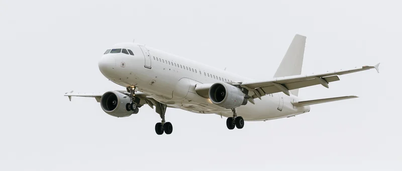 White unmarked narrow-body commercial airliner in landing approach against overcast sky