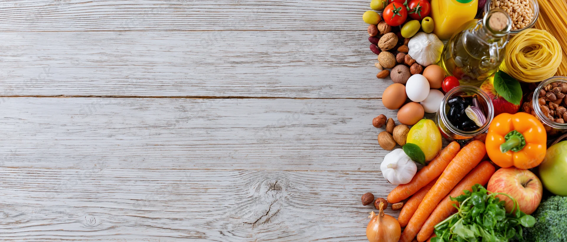 Fresh vegetables and pantry staples arranged along the right side of a white wooden surface
