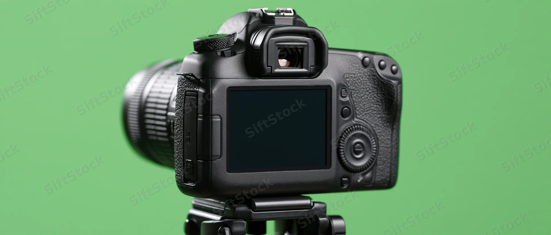 Rear view of black dslr camera mounted on tripod head against green background