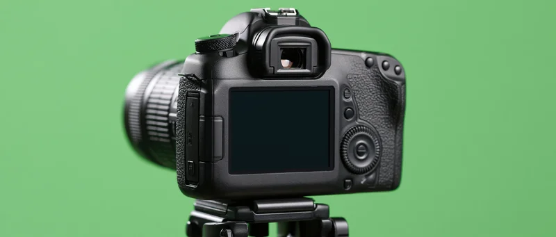 Rear view of black dslr camera mounted on tripod head against green background