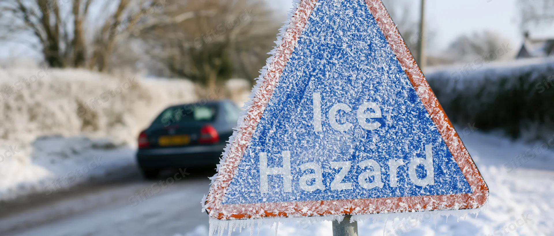 Frost-covered ice hazard warning sign on snowy roadside with car in background