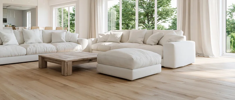 White linen sectional sofa with wooden coffee table and ottoman in bright contemporary living room with large windows and hardwood floor