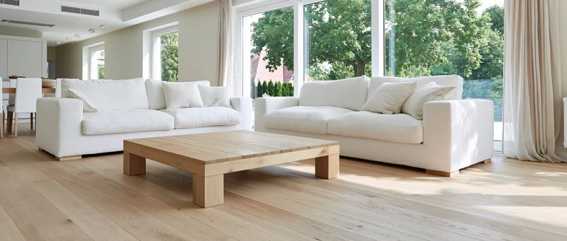 White sofas and wooden coffee table in a bright contemporary living room with large windows and hardwood flooring