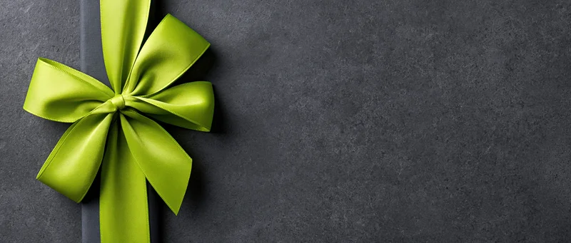 Lime green satin ribbon tied in a bow on a dark textured surface with copyspace to the right