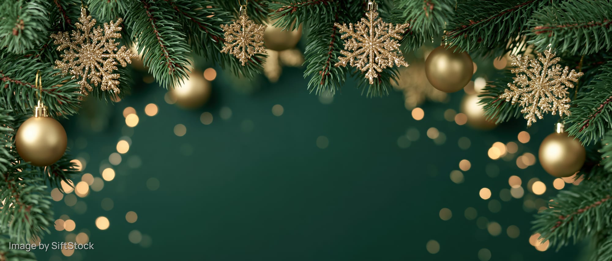 Christmas pine branches with gold ornaments and snowflakes framing a dark green background with bokeh lights and copyspace