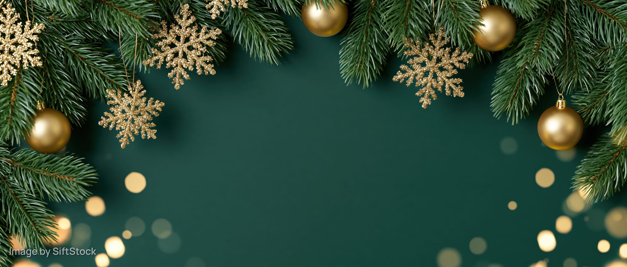 Christmas pine branches with gold ornaments and snowflakes framing a dark green background with bokeh lights and copyspace