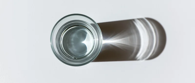 Overhead view of a clear glass of water on a white surface casting a shadow with light refraction visible