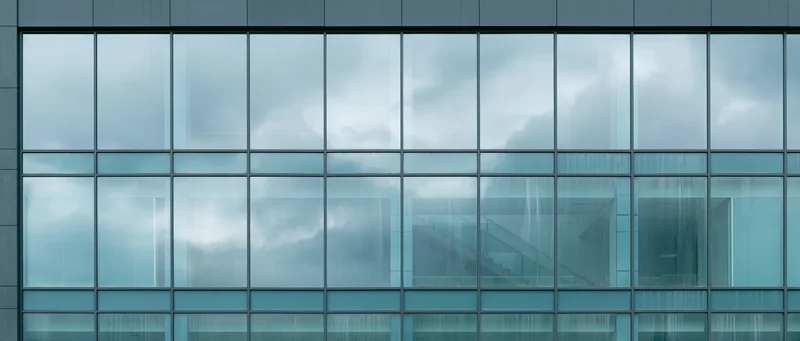 Close-up of a modern office building facade with glass curtain wall reflecting cloudy sky