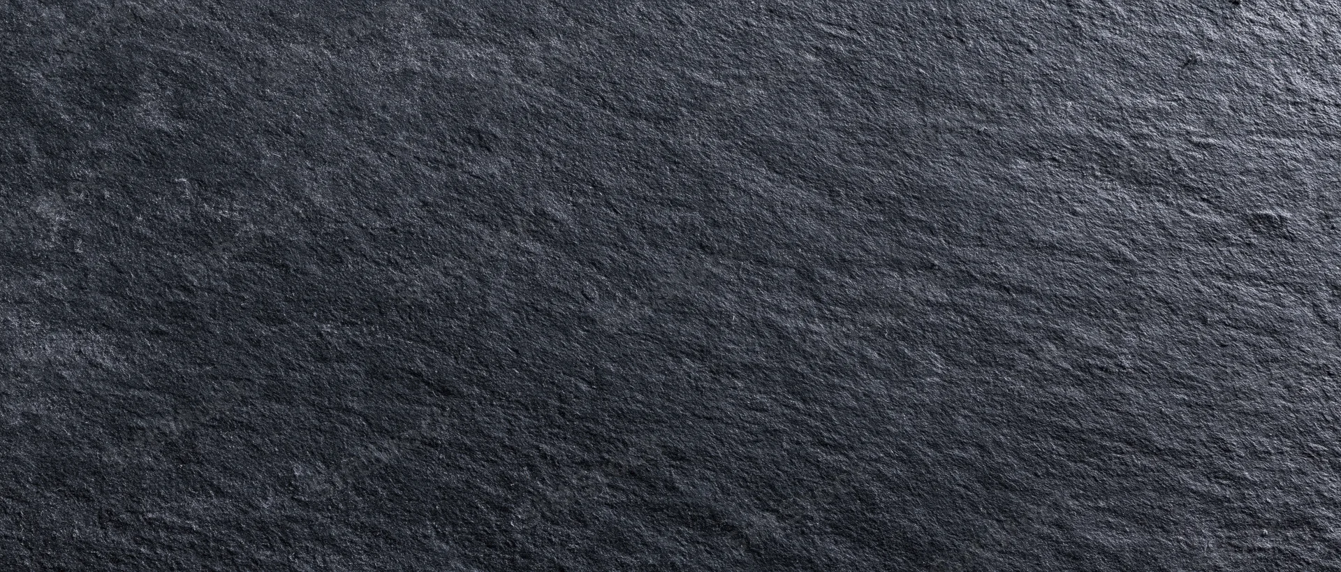 Close-up of dark charcoal blackboard surface with rough texture and natural stone grain