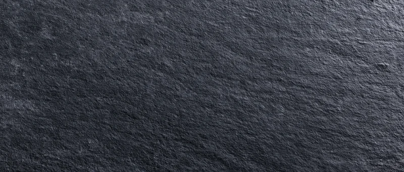 Close-up of dark charcoal blackboard surface with rough texture and natural stone grain